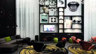 A modern lounge with black and white decor featuring a sectional sofa, stylish chairs around circular rugs, and a wall-mounted shelving unit displaying art, a bicycle, and decorative items. A screen and patterned light fixtures add to the contemporary vibe.
