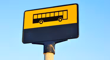 A bus stop sign with a yellow background and a black silhouette of a bus. Its mounted on a post, with a blue sky in the background.